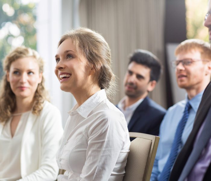 Young businesswoman and her male and female colleagues smiling, sitting and watching presentation in conference room